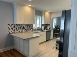 Kitchen Renovation in Cascade, MI: Bright white shaker cabinets, modern chevron tile backsplash, light grey countertops, and tiled flooring in a beautifully refinished kitchen with a dining nook view.