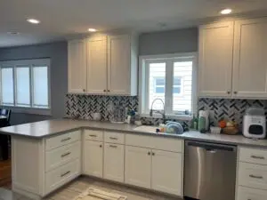 Kitchen Renovation in Ada, MI: Refinished white shaker cabinets, grey speckled countertop, stainless steel sink and dishwasher, and a dynamic black and white chevron tile backsplash.