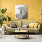 Modern living room with fresh yellow walls, neutral furniture, and plants showing the best time to book interior painting before spring