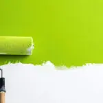 Fresh green paint being applied to an interior wall with a roller, showing why quality paint and materials matter for a smooth, long-lasting finish