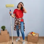 Homeowner holding a paint roller and looking concerned while painting a wall, illustrating how to tell if your home’s interior paint is failing