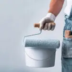 Painter holding a roller and paint bucket, illustrating what to expect from a professional interior paint job during the painting process.