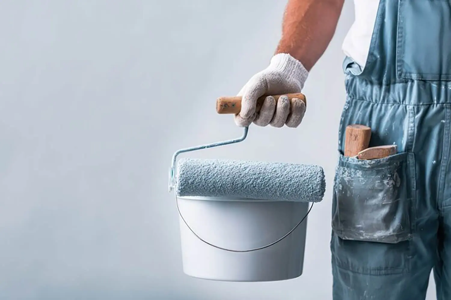 Painter holding a roller and paint bucket, illustrating what to expect from a professional interior paint job during the painting process.