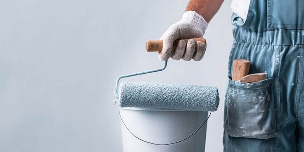 Painter holding a roller and paint bucket, illustrating what to expect from a professional interior paint job during the painting process.